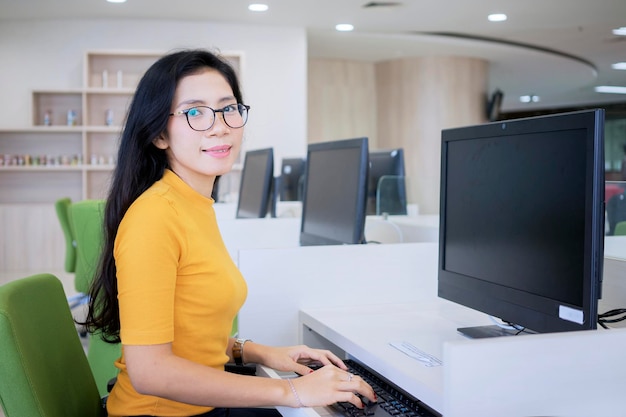 Estudante universitário fêmea que usa um computador na biblioteca