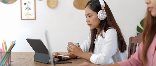 Estudante universitário feminino com aprendizagem on-line de fone de ouvido no tablet digital enquanto está sentado com sua amiga no café