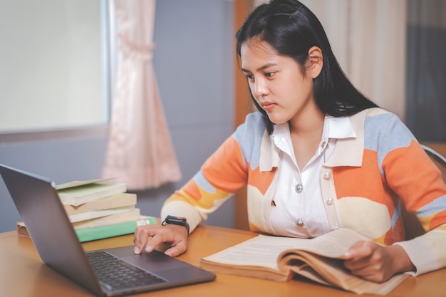 Estudante universitário jovem mulher asiática com uniforme de estudante, estudando, lendo um livro, laptop na biblioteca da universidade ou faculdade. aluna jovem e educação de tutoria com um conceito de aprendizagem tecnológica