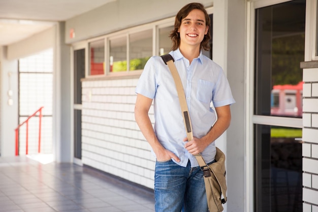 Estudante universitário masculino bonito com uma mochila de pé em um corredor e sorrindo