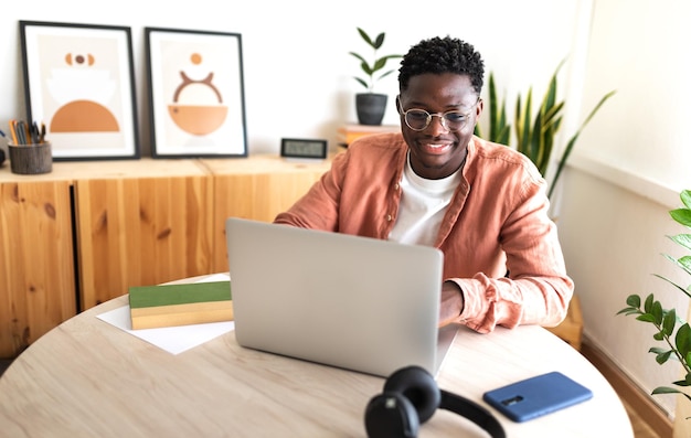 Estudante universitário negro feliz estudando em casa usando laptop