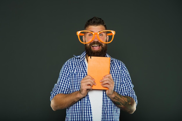 Estudante universitário nerd e engraçado com notas de aula Estudo nerd segurando livro Livro nerd usando óculos extravagantes Homem barbudo em óculos de festa com livro de lições