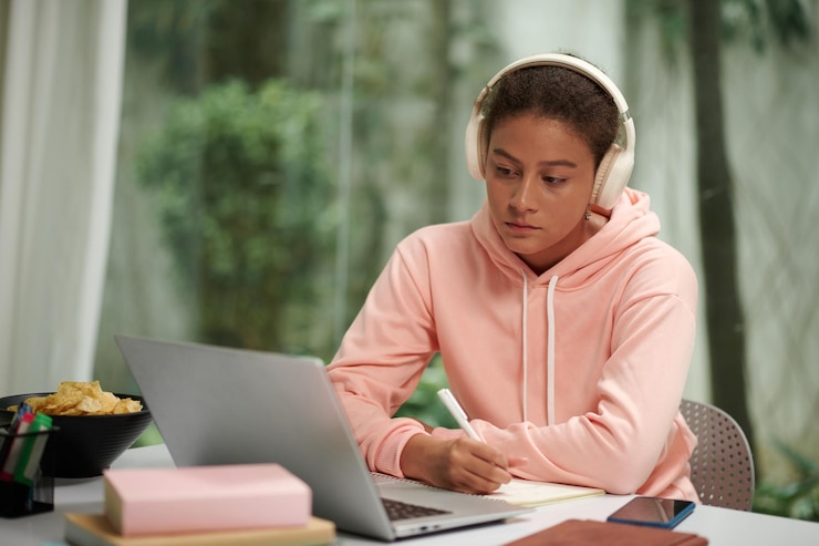 Foto estudante universitário usando fones de ouvido ao assistir a vídeos educacionais e tomar notas