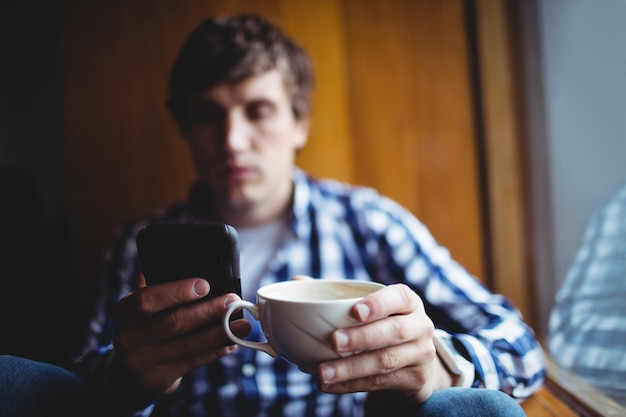 Estudante usando telefone celular enquanto tomando café