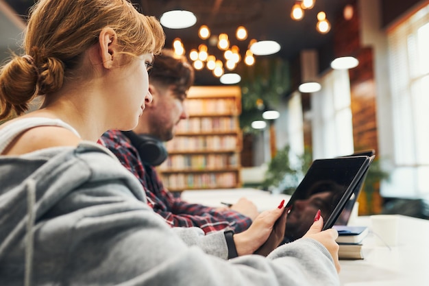 Foto estudantes a aprender na biblioteca da universidade jovem a preparar-se para um teste no portátil de volta à escola