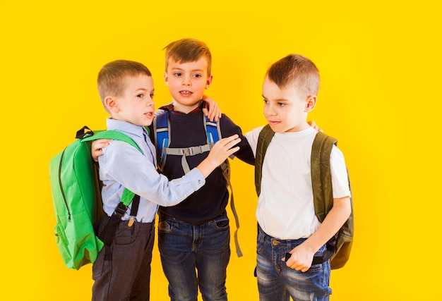 Estudantes bonitos de uniforme com mochilas em fundo amarelo