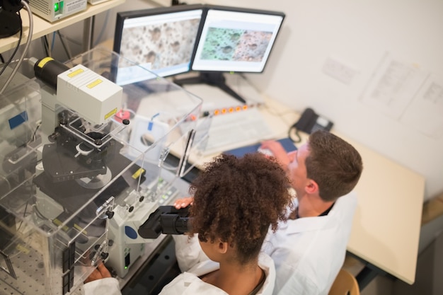 Estudantes de bioquímica usando grande microscópio e computador