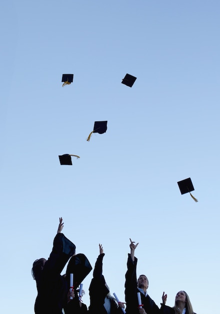 Estudantes de cinco graduados jogando seus chapéus no alto do céu