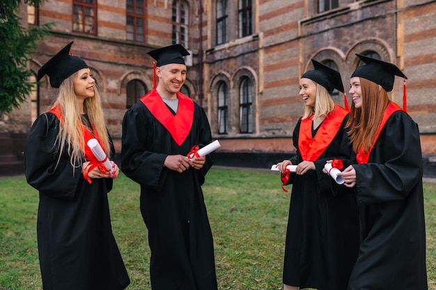 Foto estudantes de diversão divertida estão vestidos com vestidos de baile pretos colegas caminham perto da universidade após a apresentação do diploma