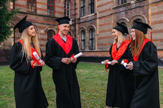 Estudantes de diversão divertida estão vestidos com vestidos de baile pretos colegas caminham perto da universidade após a apresentação do diploma