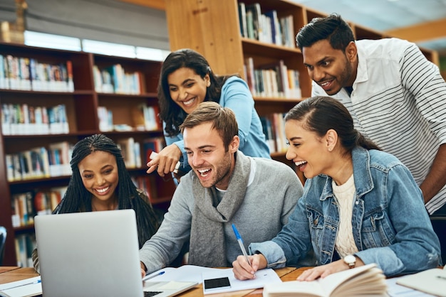 Estudantes de educação e rindo de laptop na biblioteca para projeto de pesquisa meme engraçado e tarefa criativa livros de grupo de estudo de diversidade e pessoas com aprendizagem na faculdade para preparação de testes