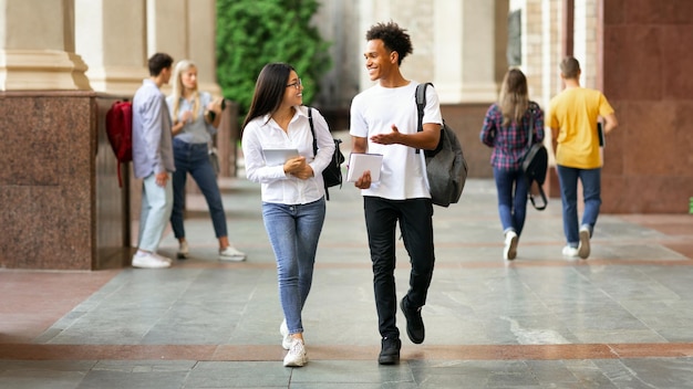 Estudantes diversos felizes caminhando no campus da faculdade durante o intervalo e conversando no espaço de cópia