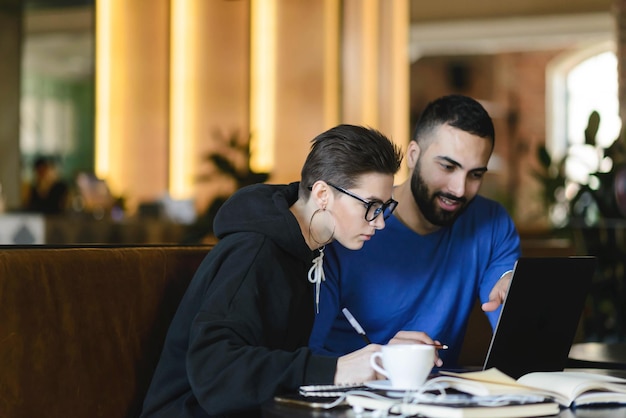 Estudantes do sexo masculino e feminino assistindo ao webinar de treinamento e fazendo anotações com informações para projeto comum