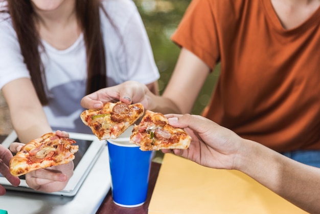 Estudantes excitados mulher e homem comendo pizza junto com pizza deliciosa de queijo. eles estão se divertindo e curtindo a festa durante o almoço na universidade ao ar livre, amigos do grupo