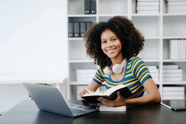 Foto estudantes femininas anotação dos livros na biblioteca de meninas africanas sentadas na mesa usando laptop e tablet para pesquisar informações on-line