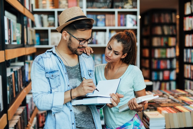 Estudantes jovens atraentes homem e mulher escolhendo livros na livraria.