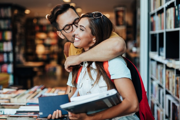 Foto estudantes jovens atraentes homem e mulher escolhendo livros na livraria.