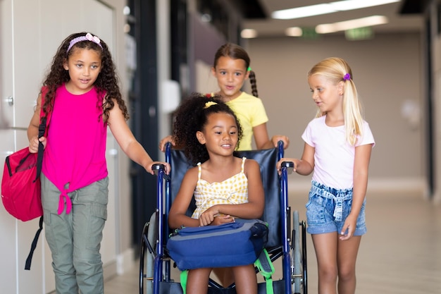 Foto estudantes multirraciais do ensino fundamental auxiliando uma colega birracial sentada em uma cadeira de rodas