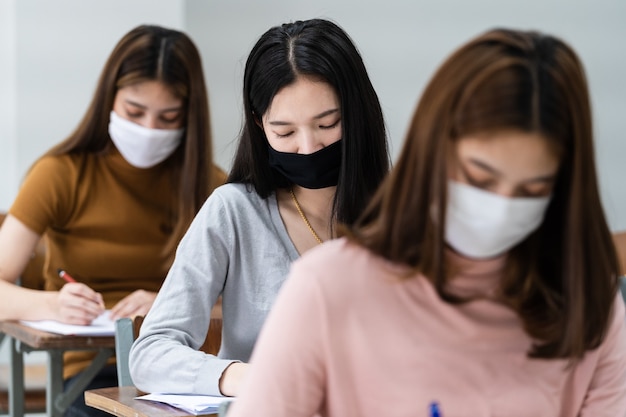 Estudantes universitárias adolescentes usam máscara facial e mantêm distância enquanto estudam em sala de aula e no campus da faculdade para prevenir a pandemia de COVID-19