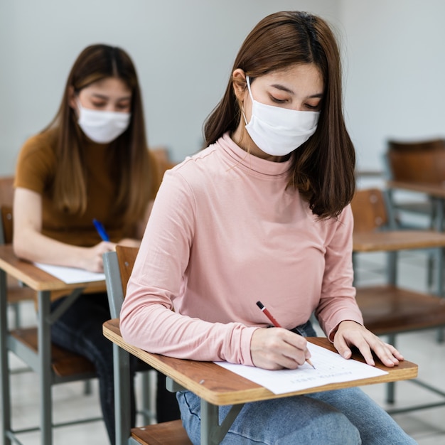 Estudantes universitárias adolescentes usam máscara facial e mantêm distância enquanto estudam em sala de aula e no campus da faculdade para prevenir a pandemia de COVID-19