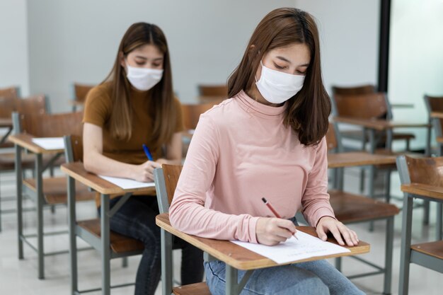 Estudantes universitárias adolescentes usam máscara facial e mantêm distância enquanto estudam em sala de aula e no campus da faculdade para prevenir a pandemia de COVID-19