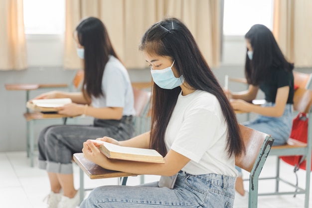 Estudantes universitários asiáticos de volta às aulas usam máscara e mantêm distância estudando na sala de aula