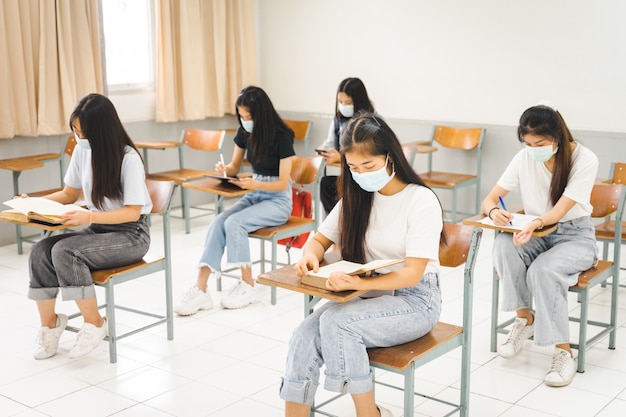 Estudantes universitários asiáticos voltam às aulas com máscara e mantêm distância social enquanto estudam em sala de aula para prevenir a pandemia de COVID-19