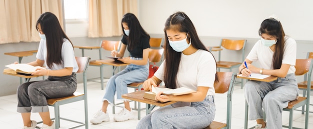 Estudantes universitários asiáticos voltam às aulas com máscara e mantêm distância social enquanto estudam em sala de aula para prevenir a pandemia de COVID-19