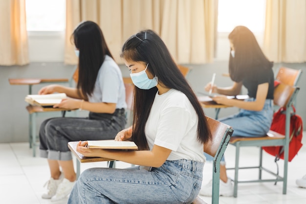 Estudantes universitários asiáticos voltam às aulas com máscara e mantêm distância social enquanto estudam em sala de aula para prevenir a pandemia de COVID-19