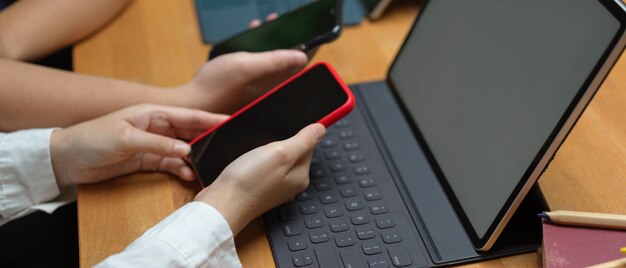 Estudantes universitários do sexo feminino navegando na internet no smartphone para encontrar informações sobre o projeto enquanto trabalham com tablet