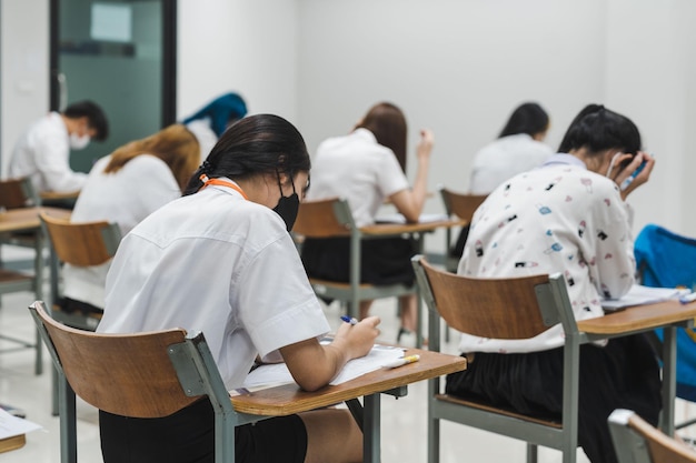 Estudantes universitários escrevendo em exames finais em sala de aula concentradoxA