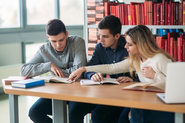 Estudantes universitários sentados juntos à mesa com livros e laptop Jovens felizes fazendo estudo em grupo na biblioteca