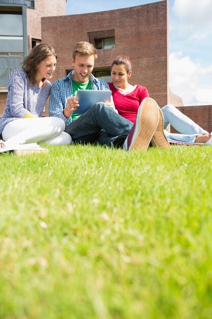 Estudantes usando tablet PC no gramado contra o edifício da faculdade