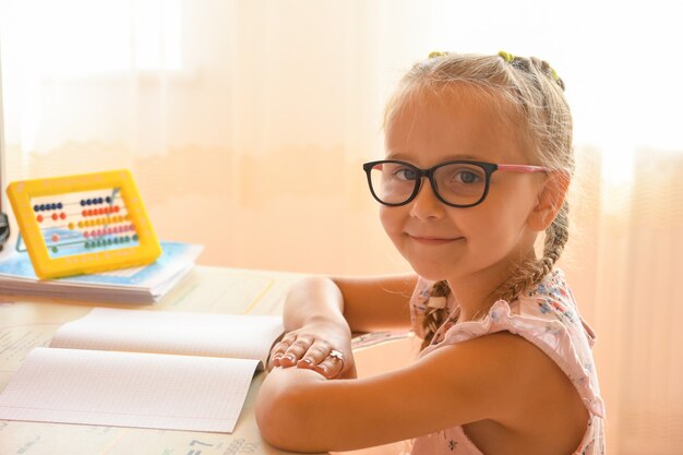 Estudiando en casa, retrato de una niña sentada en un escritorio con gafas.