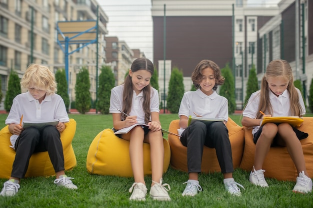 Estudiando. Niños sentados en sillas de bolsa y tomando notas