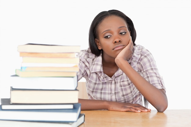 Estudiante aburrido mirando una pila de libros sobre un fondo blanco