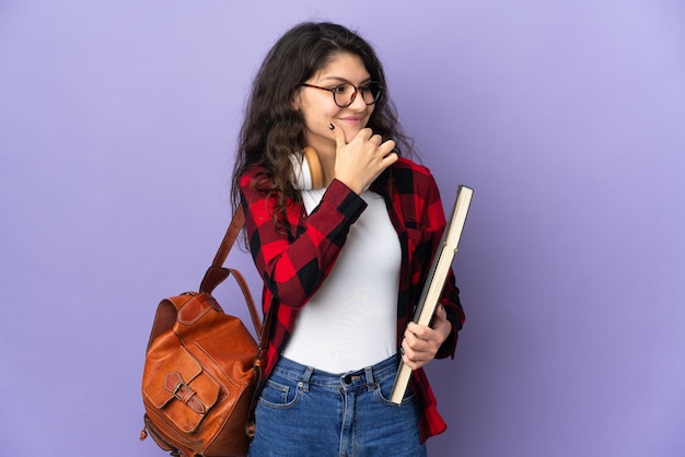 Estudiante adolescente aislado sobre fondo púrpura mirando hacia el lado y sonriendo