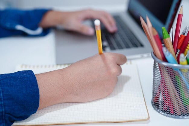 Estudiante adolescente asiático escribe la tarea con una computadora portátil aprendiendo el concepto de educación universitaria
