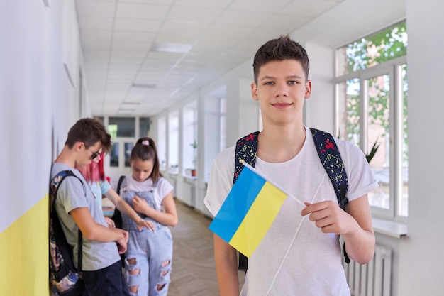 Estudiante adolescente con bandera de Ucrania, grupo de estudiantes del corredor escolar. Concepto de gente joven de educación escolar de Ucrania