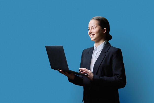 Estudiante adolescente en estilo formal usando una computadora portátil sobre un fondo azul