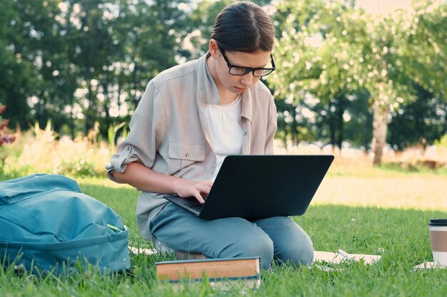 Estudiante adolescente estudiando leyendo sus libros tableta y cuaderno sentada al aire libre De vuelta a la escuela Estudiante acostada en la hierba verde usando portátil en el patio de la universidad o parque Aprendizaje a distancia