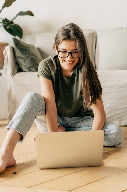 Estudiante adolescente feliz con gafas estudiando en línea desde casa usando una persona portátil