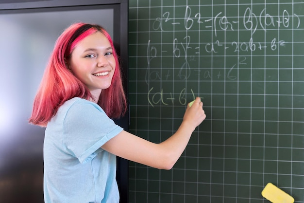 Estudiante adolescente en una lección de matemáticas escribiendo con tiza en una pizarra. Educación, adolescencia, bachillerato.