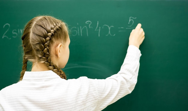 Foto estudiante adolescente en una lección de matemáticas escribiendo con tiza en una pizarra educación adolescencia