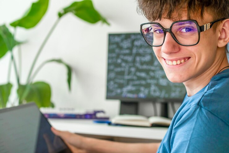 Foto estudiante adolescente lindo con gafas sentado en una computadora estudiando en línea