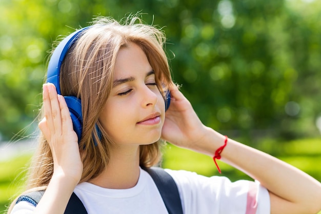 Estudiante adolescente de niña caucásica escuchando la canción favorita de música estéreo en auriculares al aire libre en el parque de la ciudad
