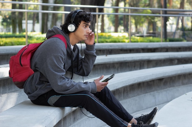 Estudiante adolescente relajándose en el parque escuchando música con auriculares