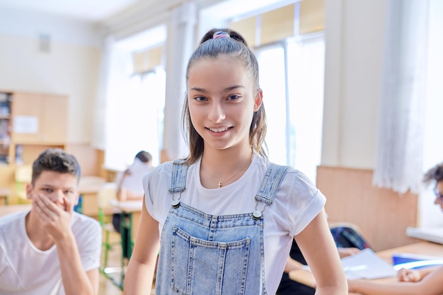 Estudiante adolescente tomando un examen, hablando mirando la cámara, aula con antecedentes de estudiantes de estudio. Escuela, educación, concepto de juventud.