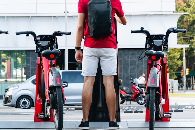 Estudiante adulto joven irreconocible alquilar una bicicleta en una gran ciudad