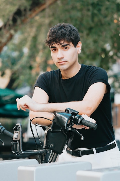 Estudiante adulto joven que alquila una bicicleta. retrato sonriendo a la cámara. Ropa moderna usando su teléfono cerca de un servicio de alquiler de bicicletas, desbloqueando bicicletas de alquiler para moverse por la ciudad, servicios de alquiler